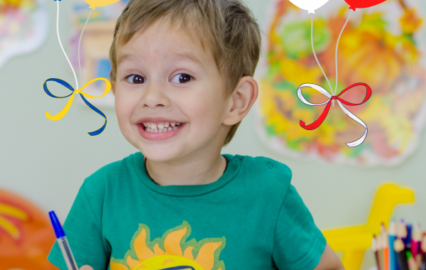 Uśmiechnięty chłopczyk w trakcie rysowania. Nad nim balony w barwach Polski i Ukrainy