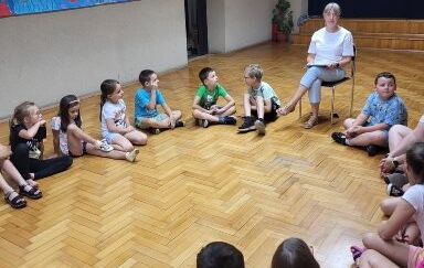 Dzieci siedzące na podłodze i słuchające bibliotekarki