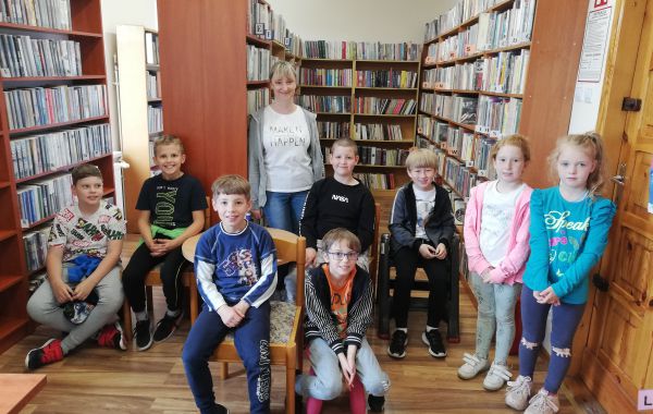 Bibliotekarz z dziećmi pozujący do wspólnego zdjęcia na tle regałów z książkami