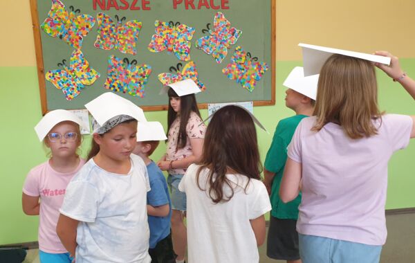 Dzieci w kółku próbujące utrzymać kartkę papieru na głowie
