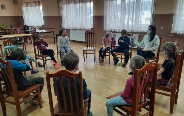 Uczestnicy spotkania siedzący na krzesłach w okręgu i słuchający czytanej opowieści
